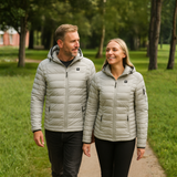 Man and woman wearing matching light gray puffer jackets in a park.