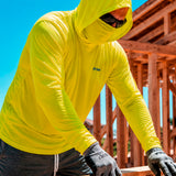 Man wearing a hi-vis yellow GOBI Helio UPF Sun Hoodie with hood and built-in face cover pulled up at a construction site, with wood framing in the background.