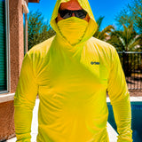 Man standing poolside in a hi-vis yellow Gobi Helio UPF Sun Hoodie with hood and face cover up, wearing sunglasses with a pool and palm trees behind him.