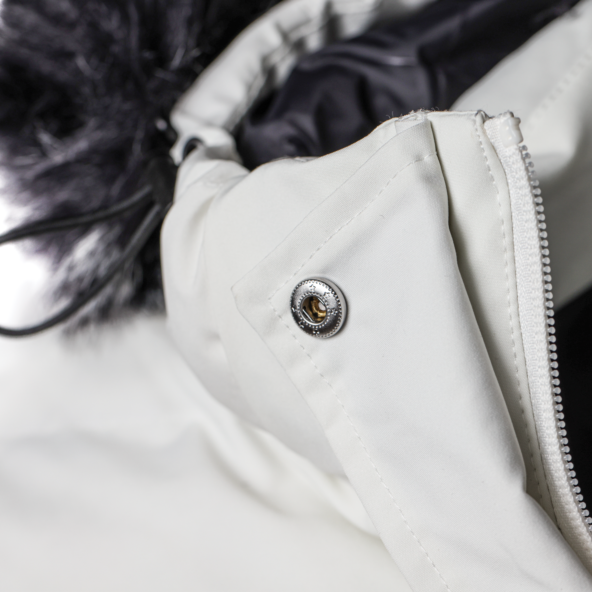 Close-up of a white jacket with a button and zipper detail.